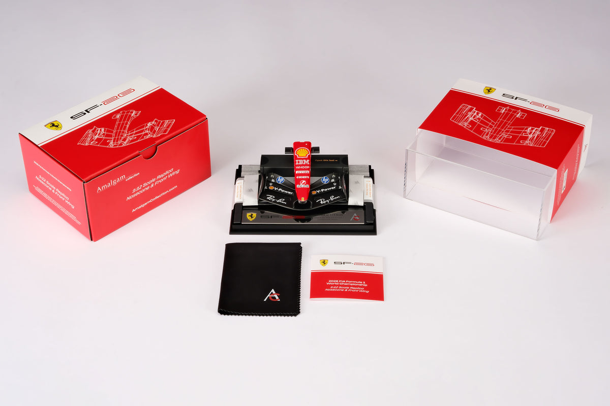 A miniature model of a red and black Formula 1 Ferrari SF-26 nosecone, mounted on a black display base surrounded by packaging, against a neutral grey studio background.