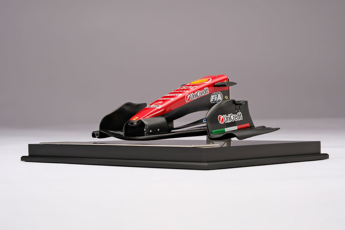 A miniature model of a red and black Formula 1 Ferrari SF-26 nosecone, mounted on a black display base against a neutral grey studio background.