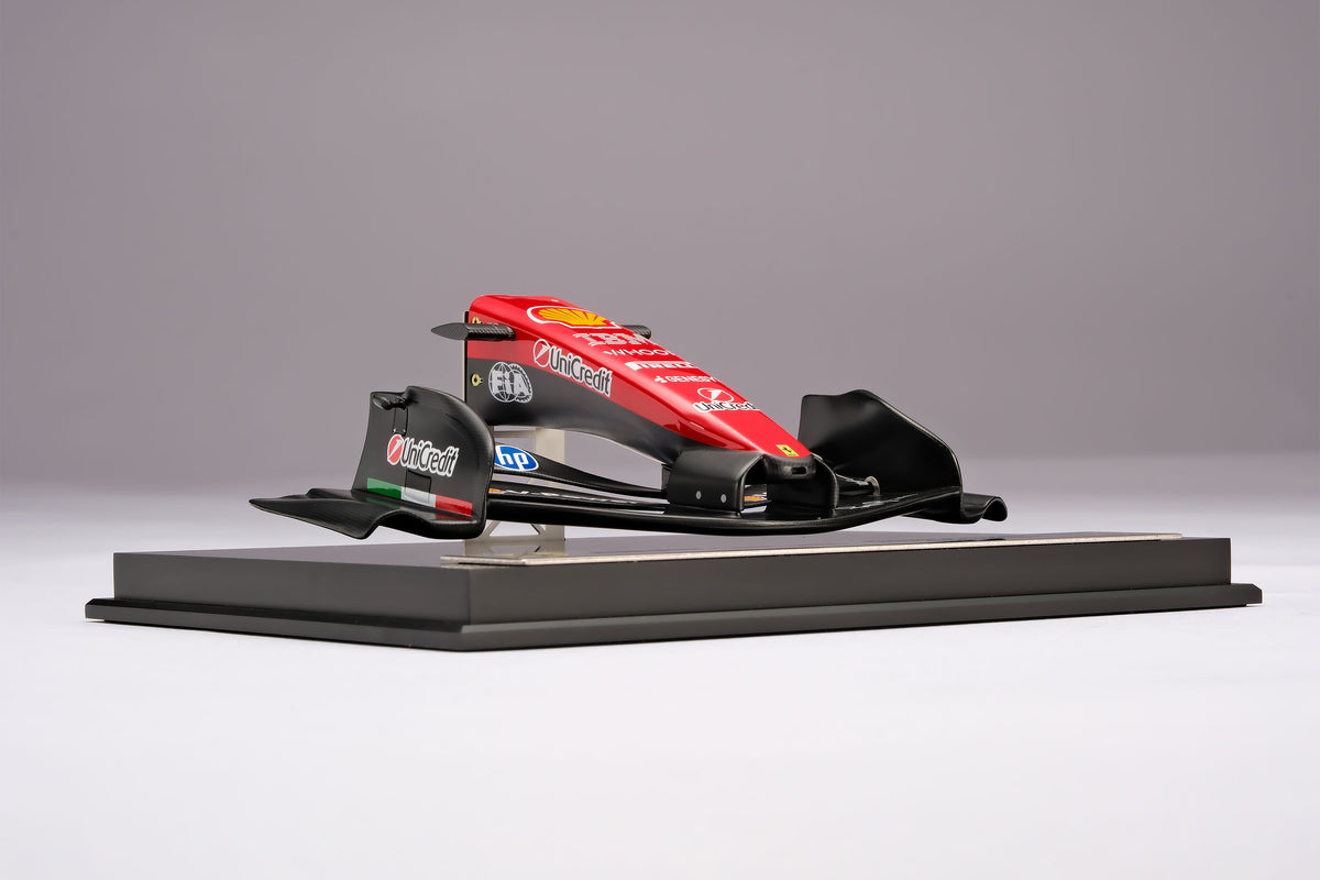 A miniature model of a red and black Formula 1 Ferrari SF-26 nosecone, mounted on a black display base against a neutral grey studio background.
