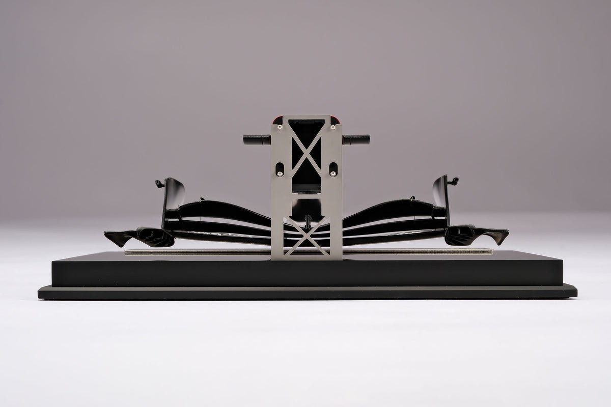 A miniature model of a red and black Formula 1 Ferrari SF-26 nosecone, mounted on a black display base against a neutral grey studio background.