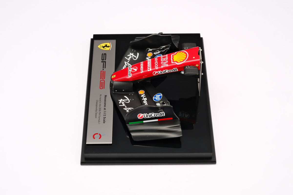 A miniature model of a red and black Formula 1 Ferrari SF-26 nosecone, mounted on a black display base, against a neutral grey studio background.