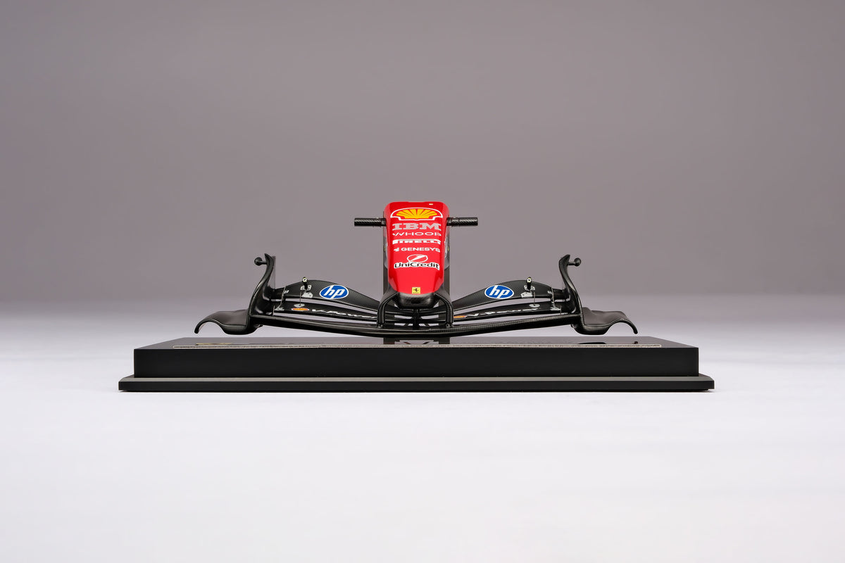 A miniature model of a red and black Formula 1 Ferrari SF-26 nosecone, mounted on a black display base against a neutral grey studio background.