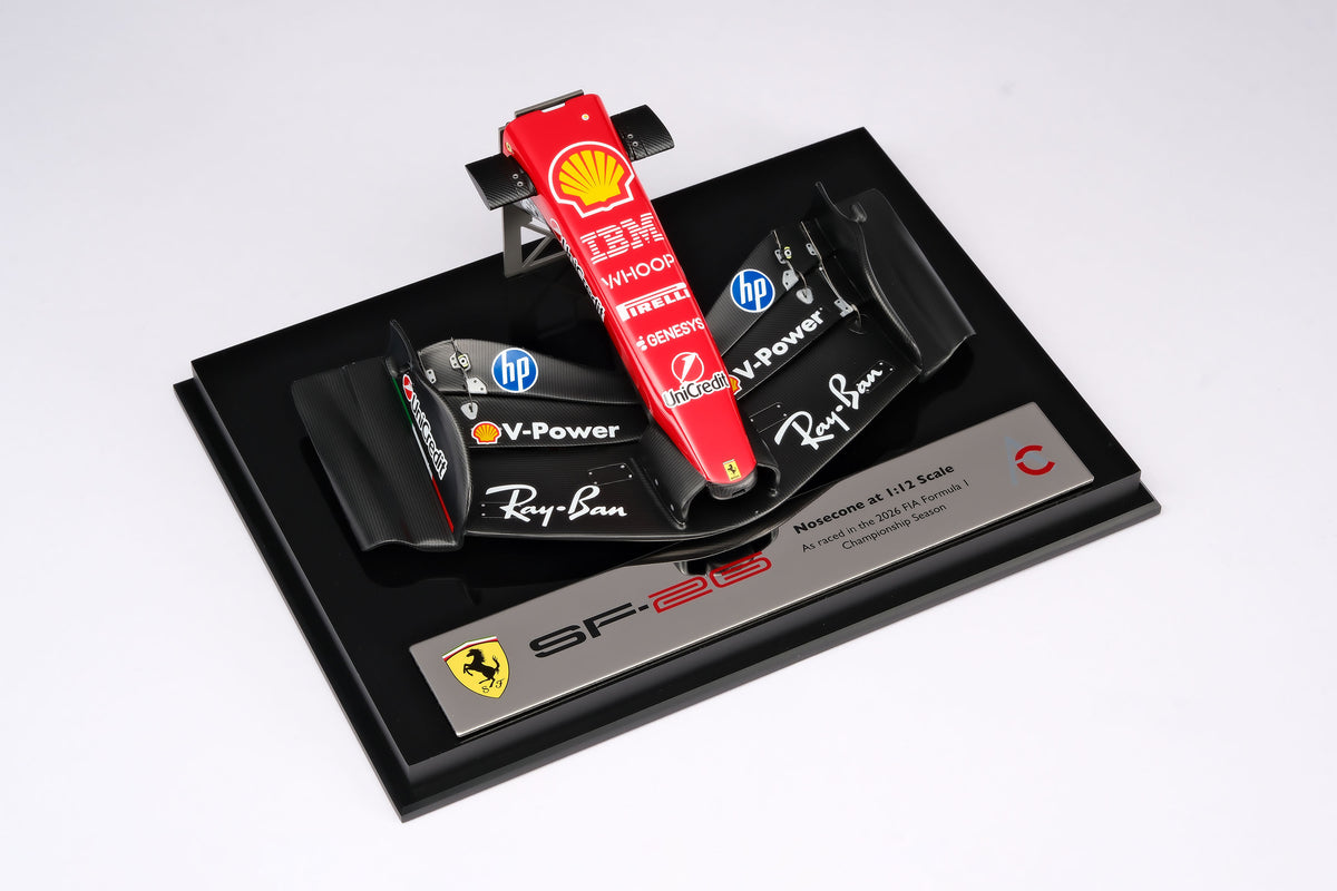 A miniature model of a red and black Formula 1 Ferrari SF-26 nosecone, mounted on a black display base, against a neutral grey studio background.