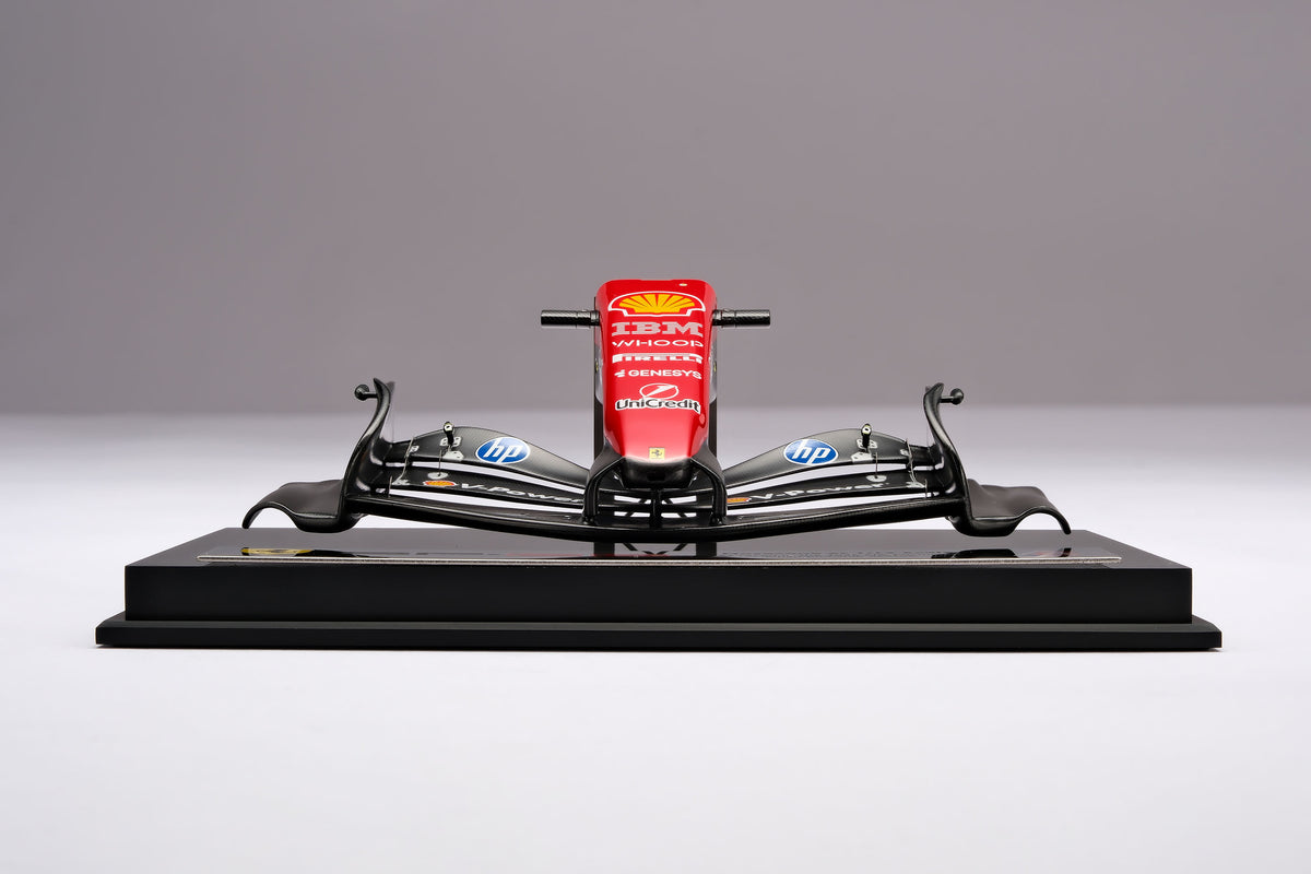 A miniature model of a red and black Formula 1 Ferrari SF-26 nosecone, mounted on a black display base, against a neutral grey studio background.