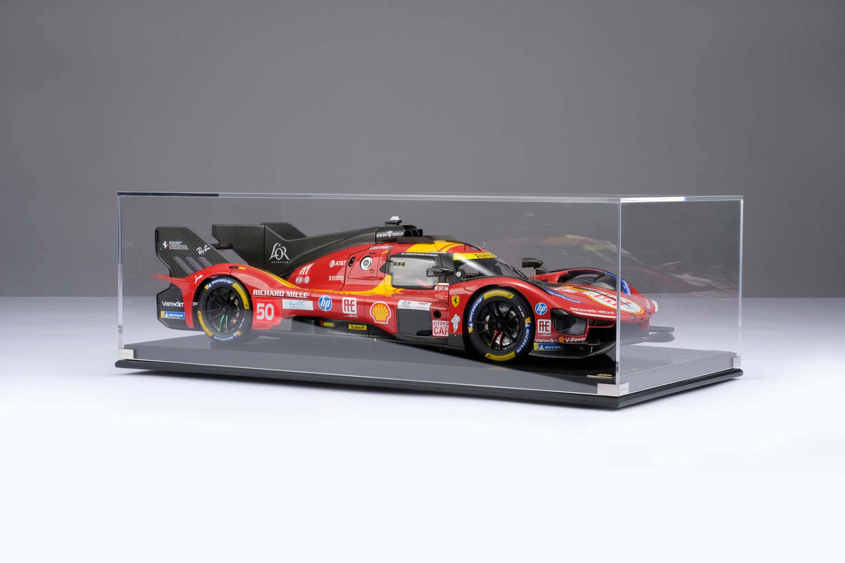 A red and yellow Ferrari 499P 2025 Le Mans racing car at 1.8 scale inside a glass display box and displayed on a light surface.