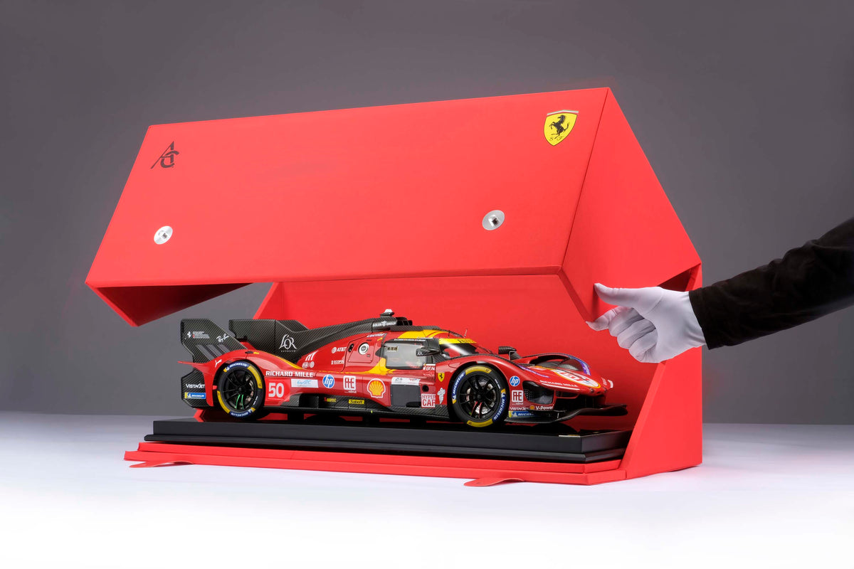 A shot of a Ferrari 499P 2025 Le Mans racing car at 1.8 scale with multiple sponsors, displayed in a box on a light surface.