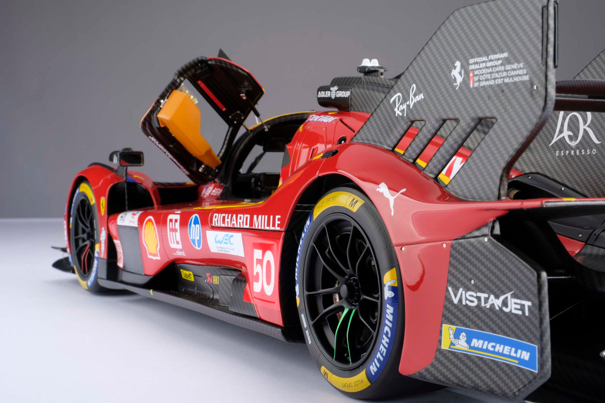 A detail shot of a red and yellow Ferrari 499P 2025 Le Mans racing car at 1.8 scale with multiple sponsors, displayed on a light surface.