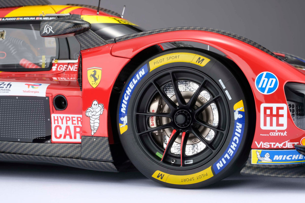 A close up shot of the tire of a Ferrari 499P 2025 Le Mans racing car at 1.8 scale with multiple sponsors, displayed on a light surface.