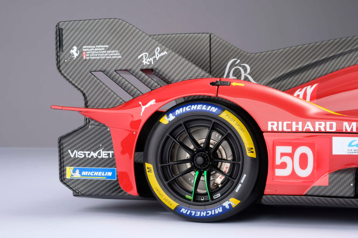 A close up shot of the tire of a Ferrari 499P 2025 Le Mans racing car at 1.8 scale with multiple sponsors, displayed on a light surface.